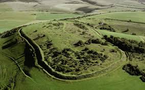 Aerial view of a circular grassy hill fort with a surrounding ditch.