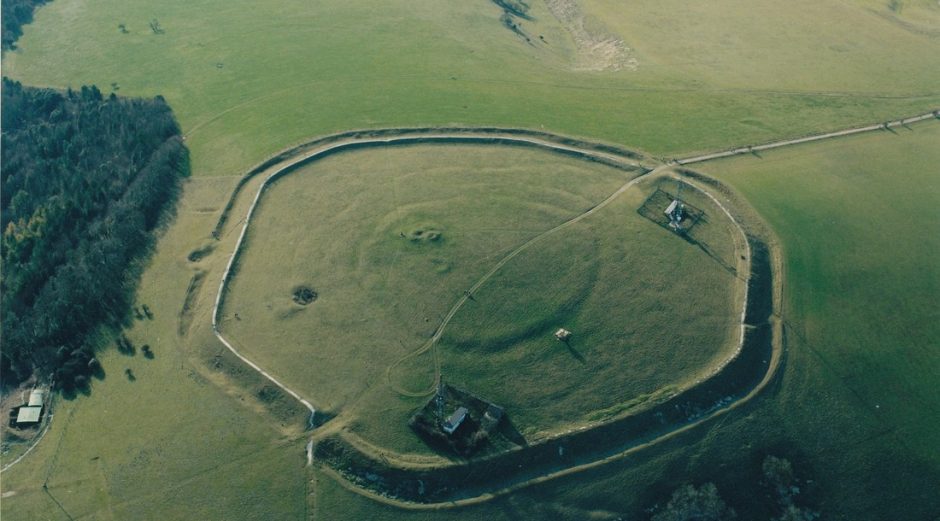 Aerial view of a circular hill fort with a surrounding ditch in a grassy field.