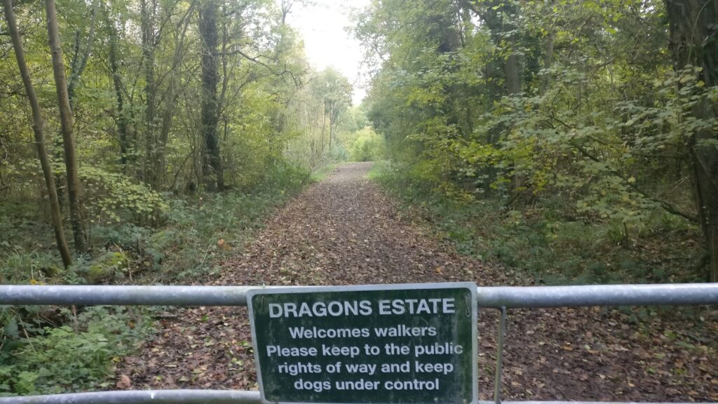 A wooded trail blocked by a metal gate with a sign for Dragons Estate.
