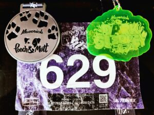 Race bib number 629 with two medals hanging above it—a white circular paw-print medal on the left and a bright green cloud-shaped medal on the right.