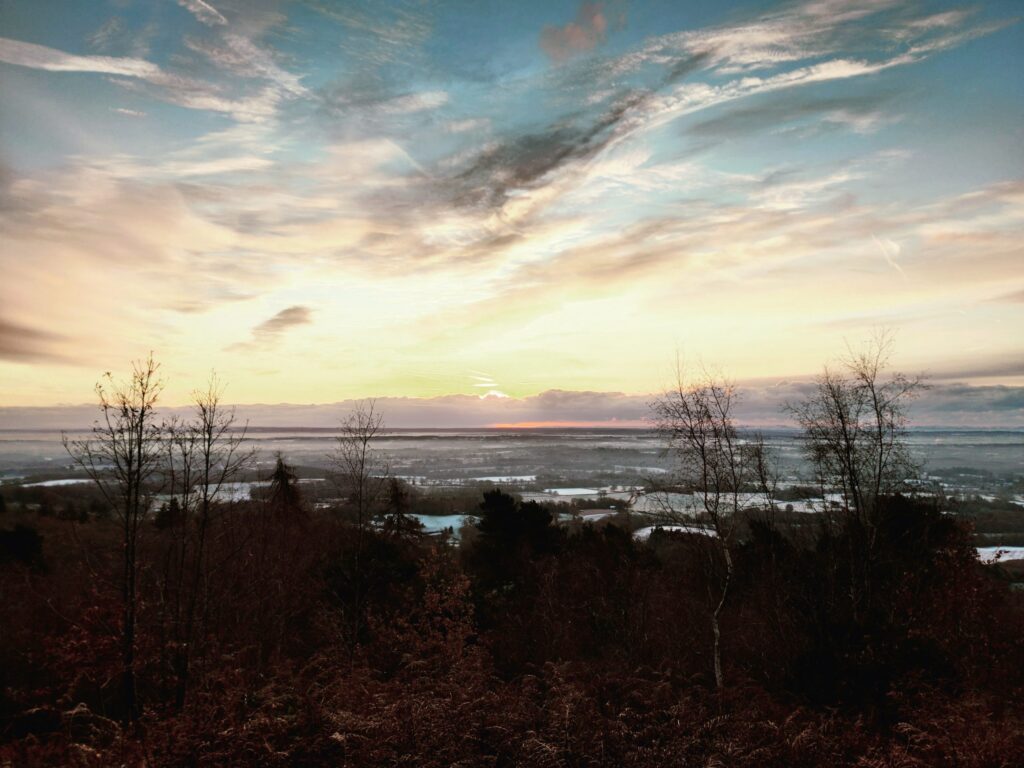 Sunset over a calm lake with bare trees along the shore and a colorful sky.