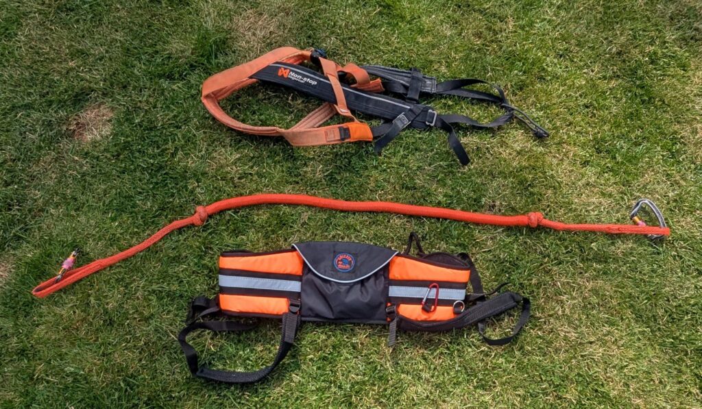 Two orange and black safety harnesses lying on grass.